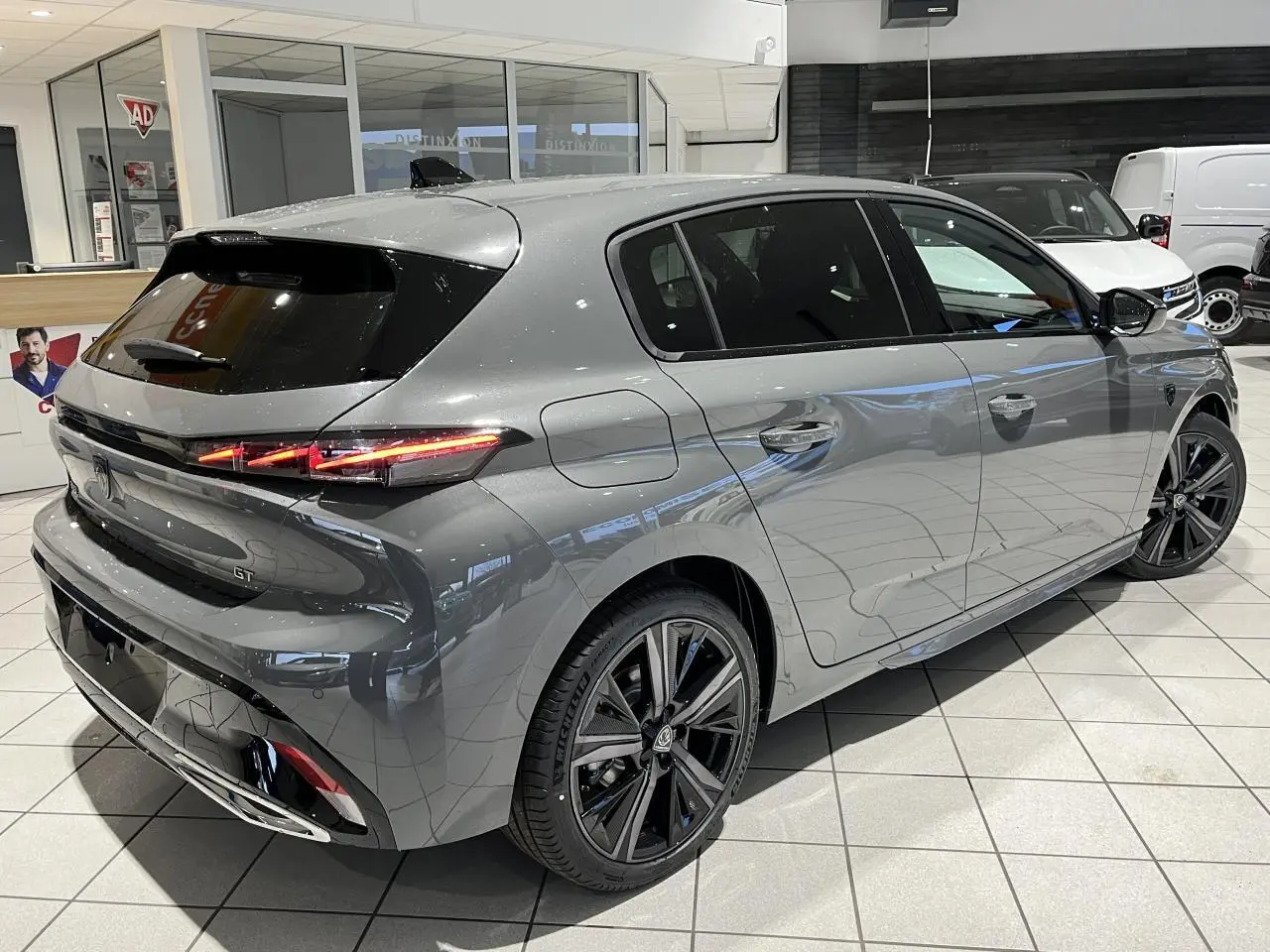 Peugeot 308 GT gris sélénium vue 3/4 arrière droit en intérieur avec jantes alliage noires et feux LED distinctifs.