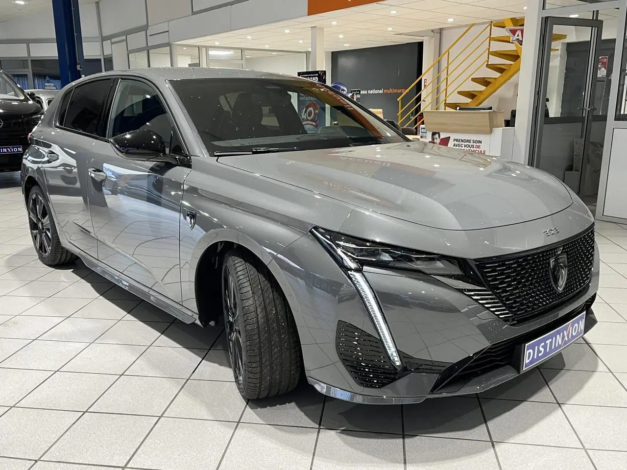 PEUGEOT 308 gris selenium en 3/4 avant droit, avec calandre noire brillante et feux LED griffés.