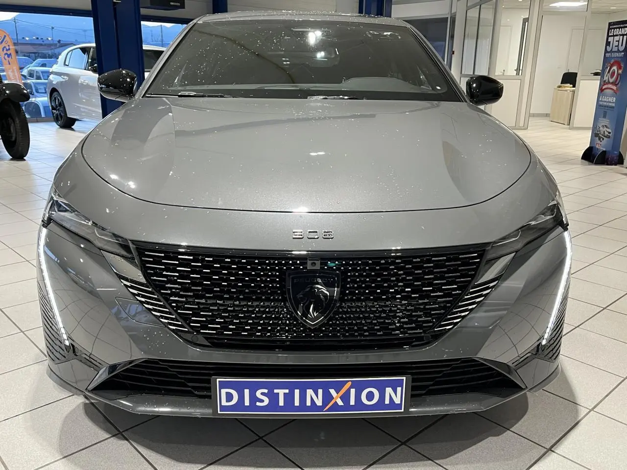 Vue de face d'une Peugeot 308 gris sélénium avec calandre noire brillante et feux LED dynamiques en showroom.
