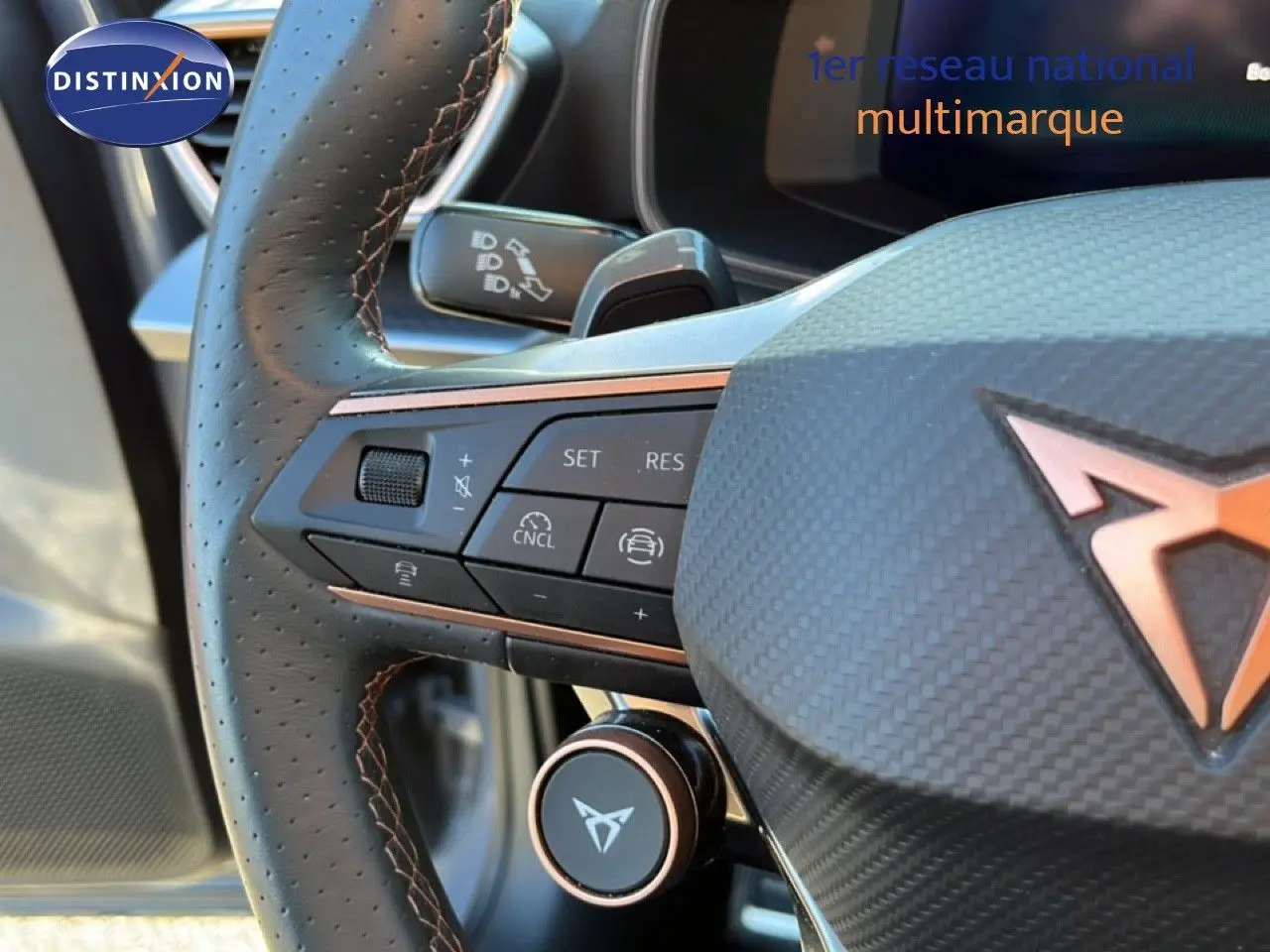 Gros plan sur le volant en cuir perforé noir avec surpiqûres cuivrées et logo CUPRA en relief cuivré.