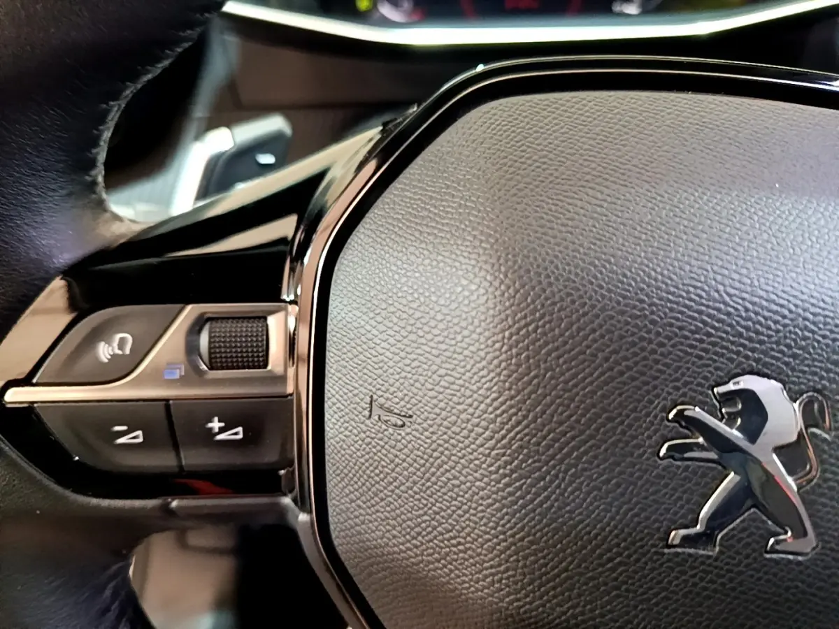 Gros plan sur le volant cuir noir multifonctions du Peugeot 2008 blanc, avec logo lion chromé visible au centre.