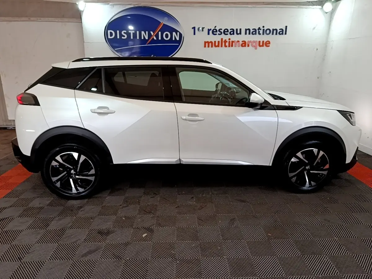 Vue de profil côté gauche d'un Peugeot 2008 blanc 2021 avec jantes noires et toit noir, dans un showroom intérieur.