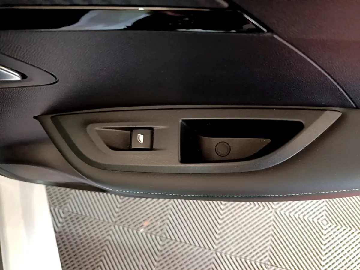 Gros plan sur la commande de lève-vitre côté gauche de la porte intérieure noire d’un Peugeot 2008 blanc.
