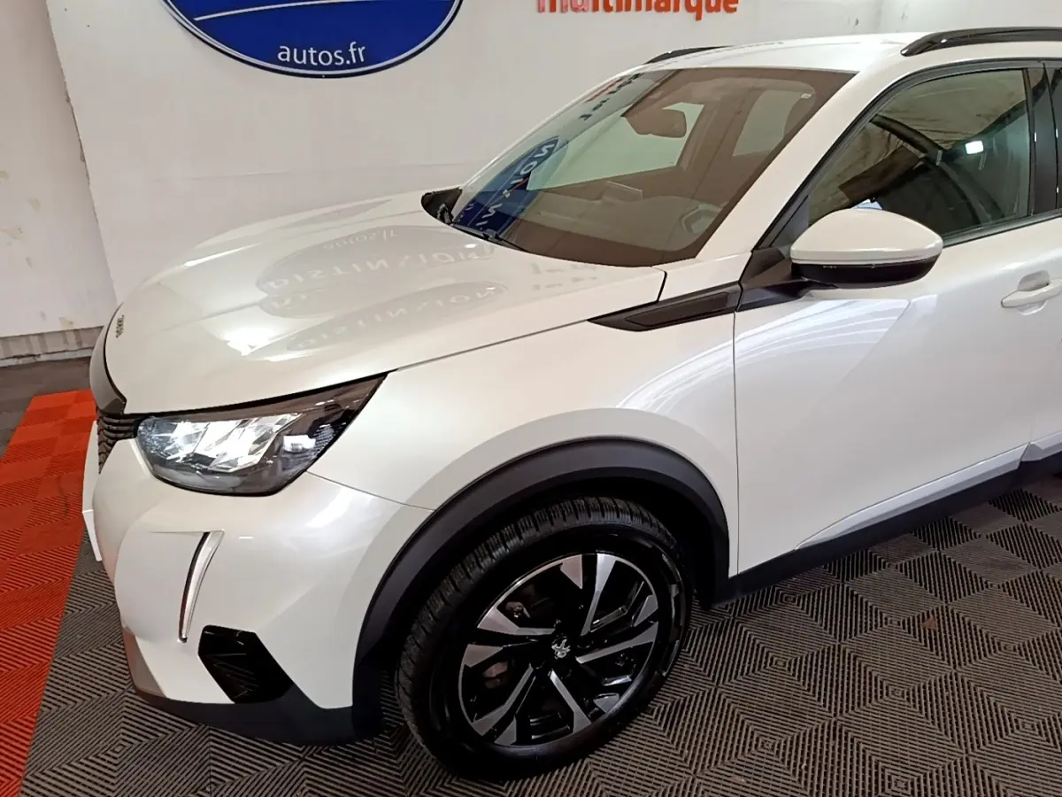 Vue 3/4 avant droit d'un Peugeot 2008 blanc avec jantes noires et détails noirs contrastants sur ailes et rétroviseur.