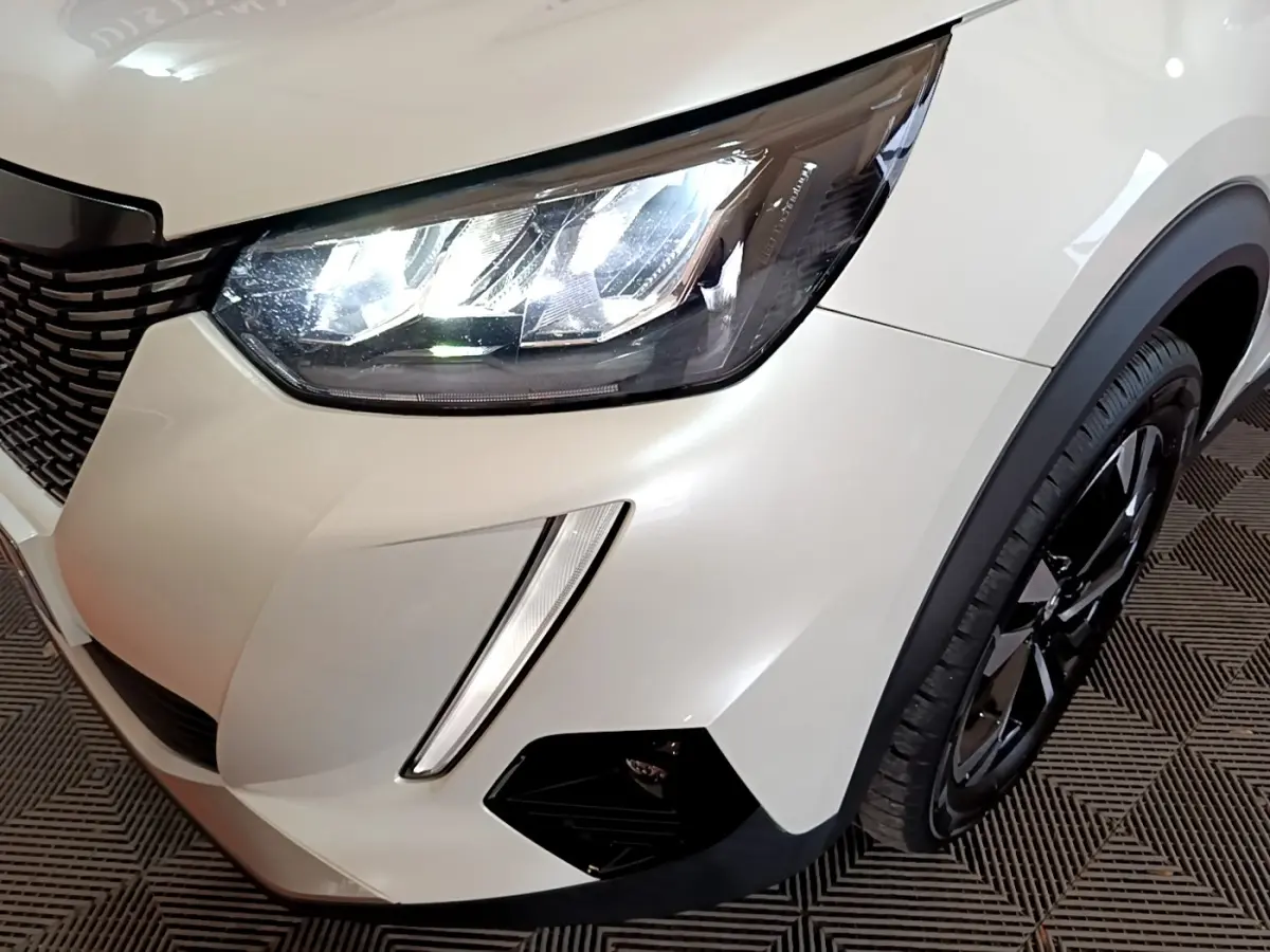 Gros plan sur l'avant droit blanc du Peugeot 2008 2021, mettant en valeur le phare LED et la roue noire brillante.