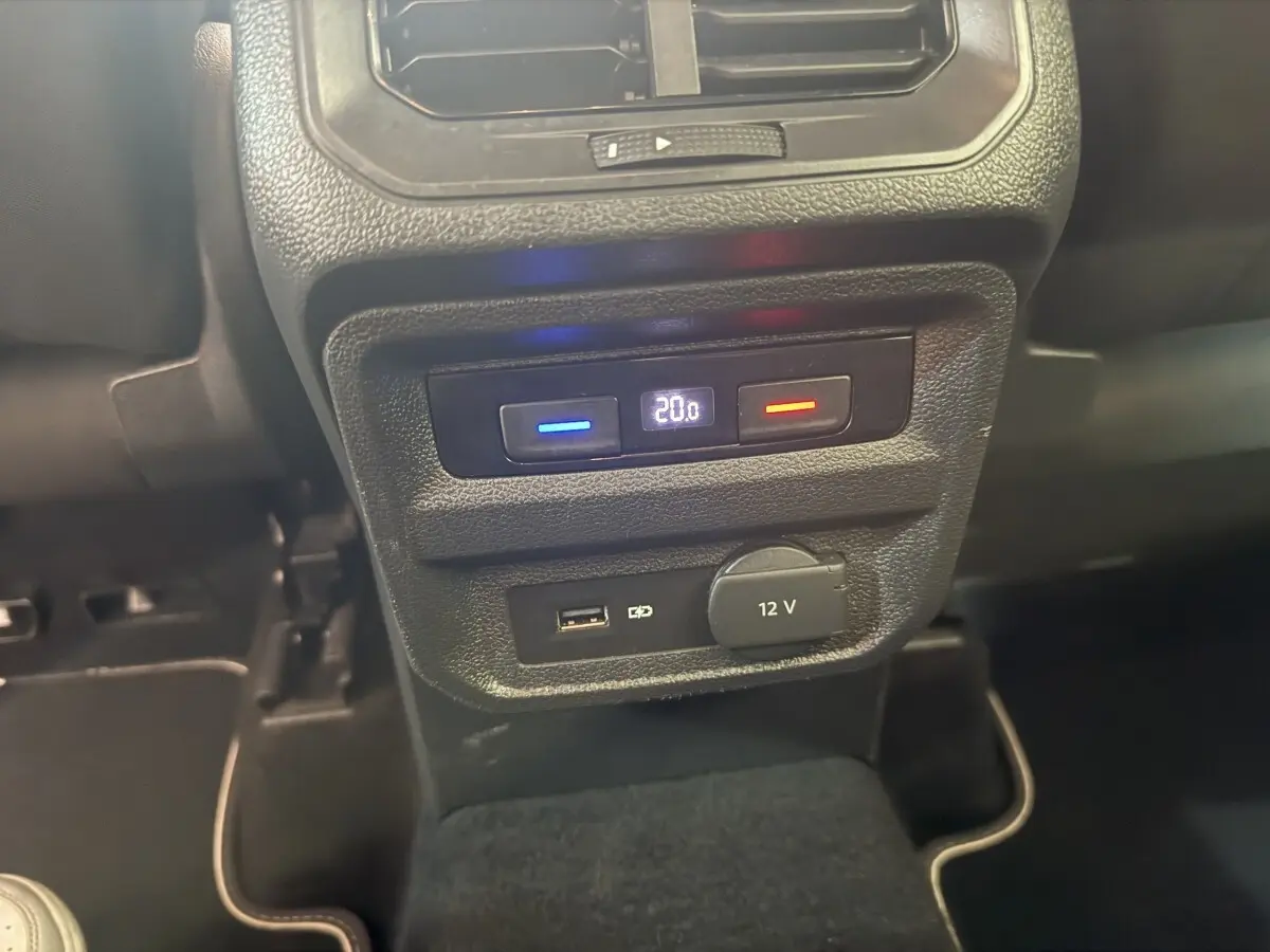 Gros plan sur la console arrière du Volkswagen Tiguan gris clair, avec commandes climatisation et prises USB et 12V visibles.