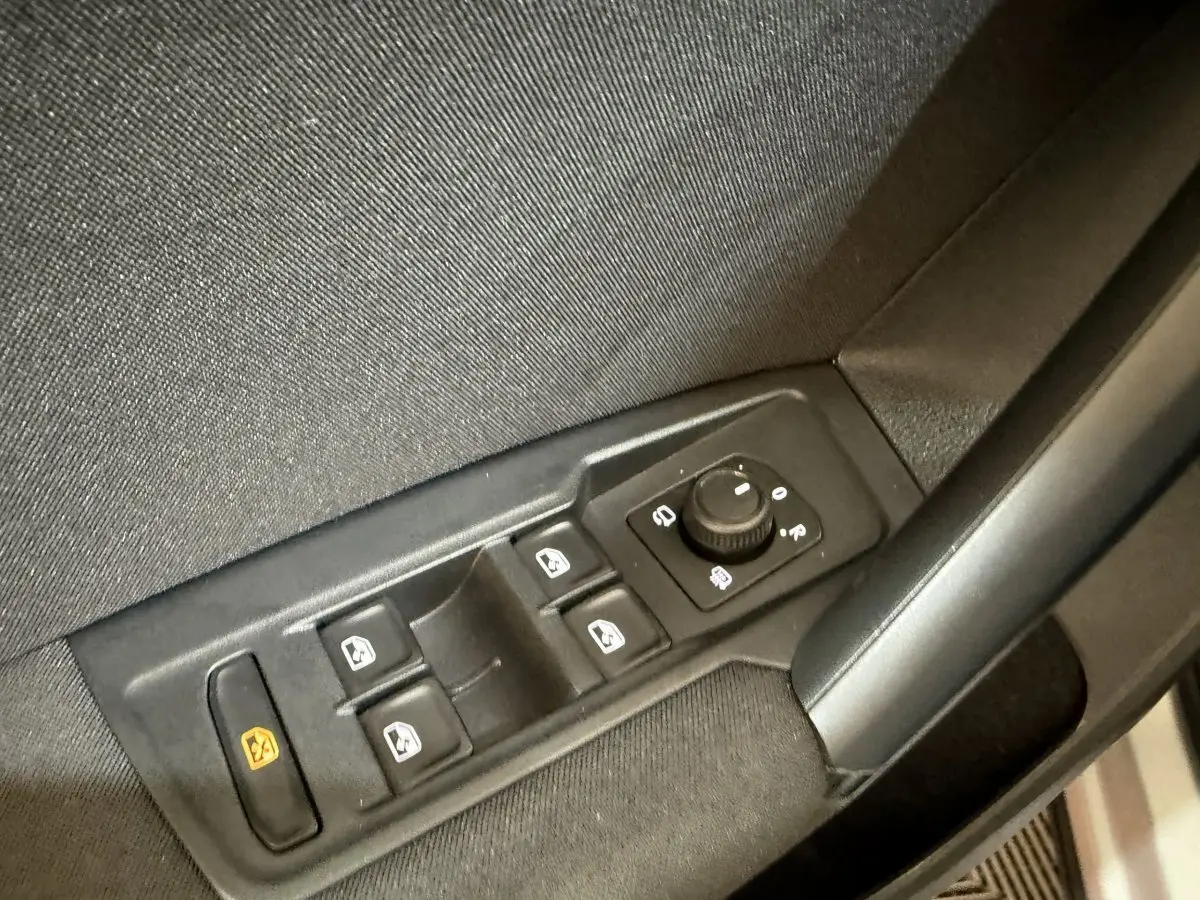 Vue rapprochée des commandes de lève-vitres et rétroviseurs sur la porte côté conducteur d’un Volkswagen Tiguan gris clair.