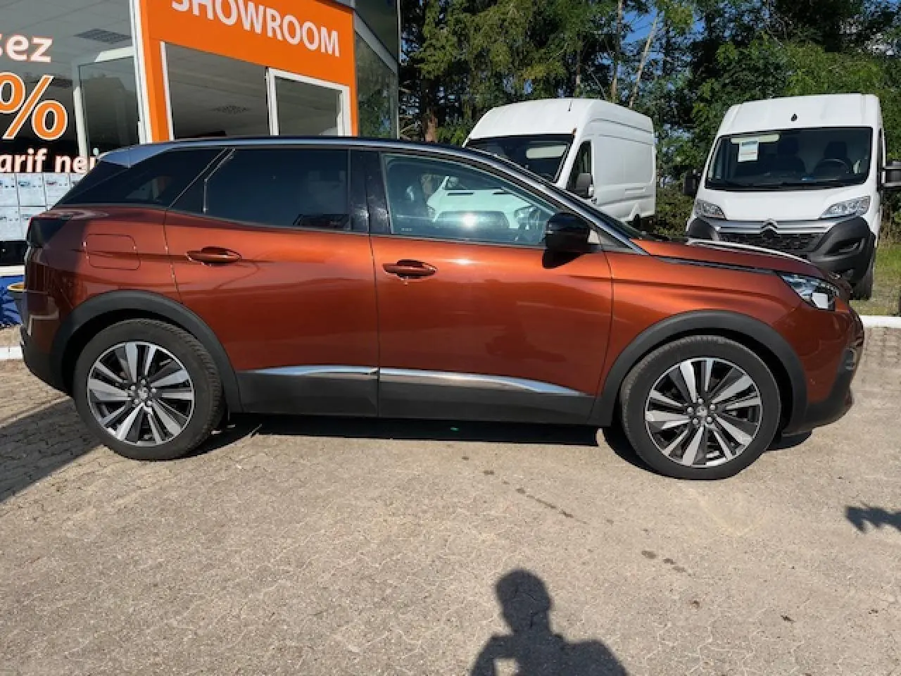 Profil côté gauche d'un Peugeot 3008 2016 métallisé cuivre avec jantes alliage, garé devant un showroom.