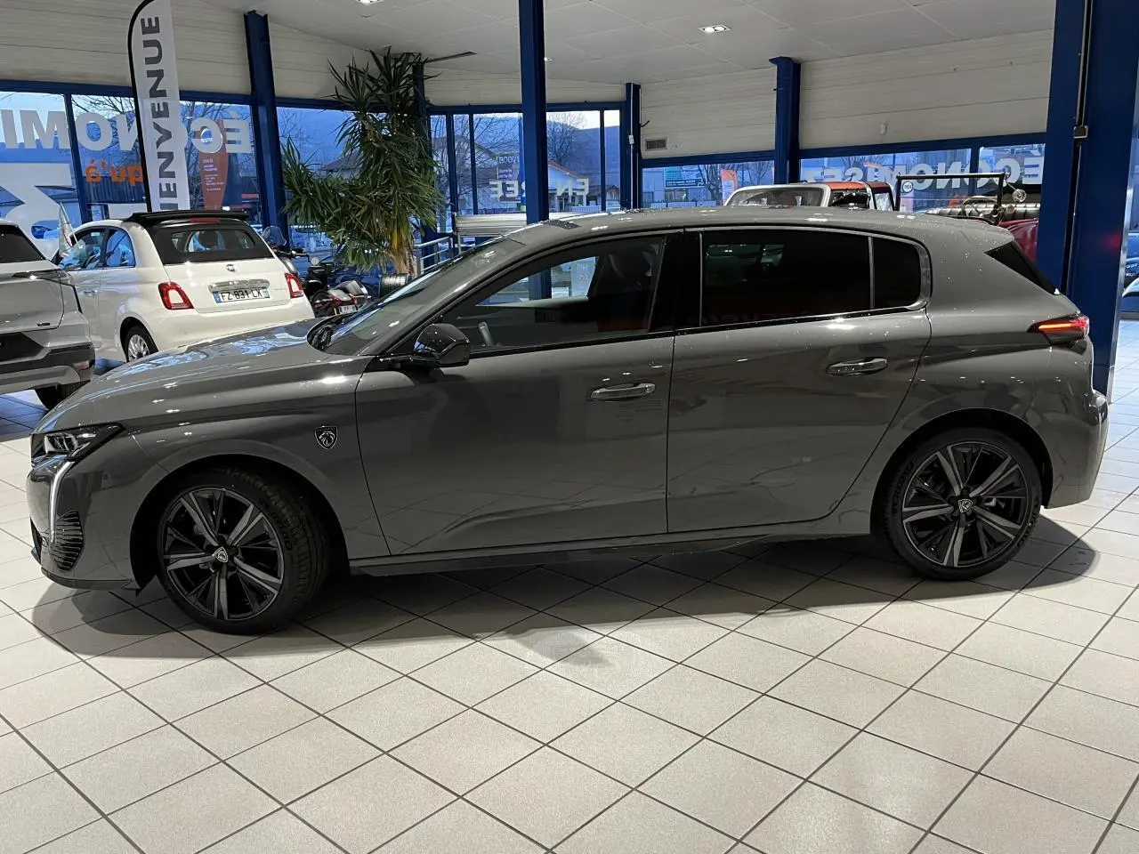 Profil côté gauche d'une Peugeot 308 gris selenium 2024 en berline GT avec jantes alliage noires en showroom.