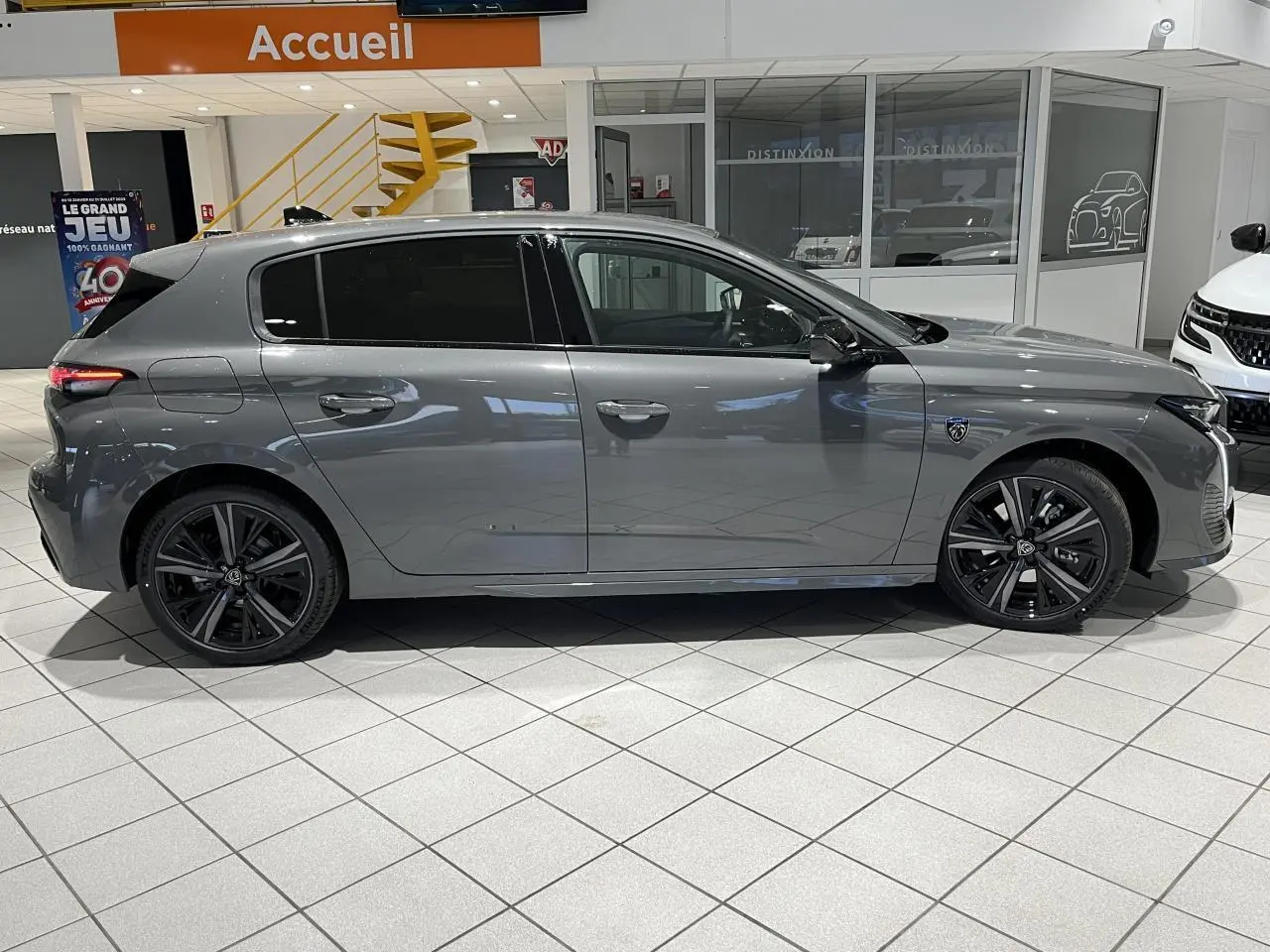 Profil côté gauche d'une Peugeot 308 gris sélénium 2024 en berline GT avec jantes alliage noires en showroom.