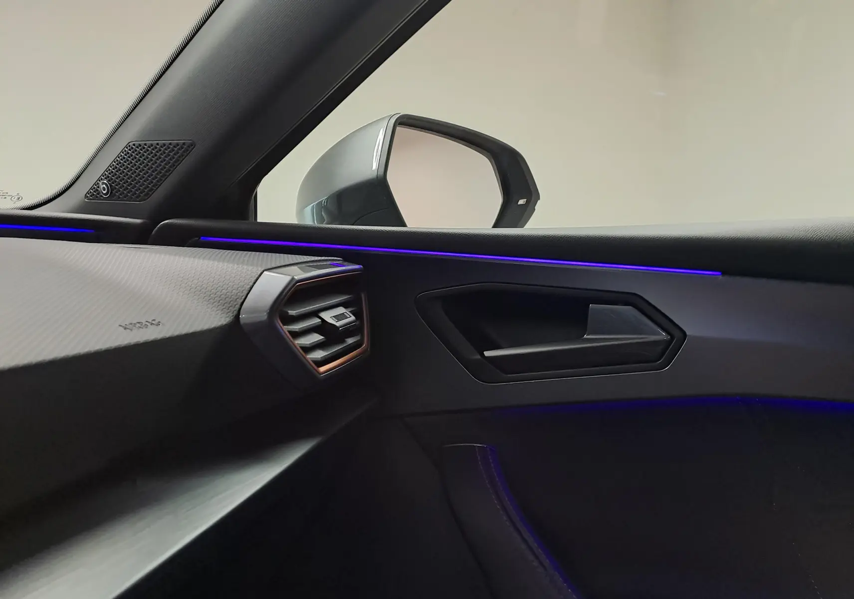 Vue intérieure côté passager de la CUPRA Leon 2023, avec éclairage d'ambiance bleu et garnitures noires.