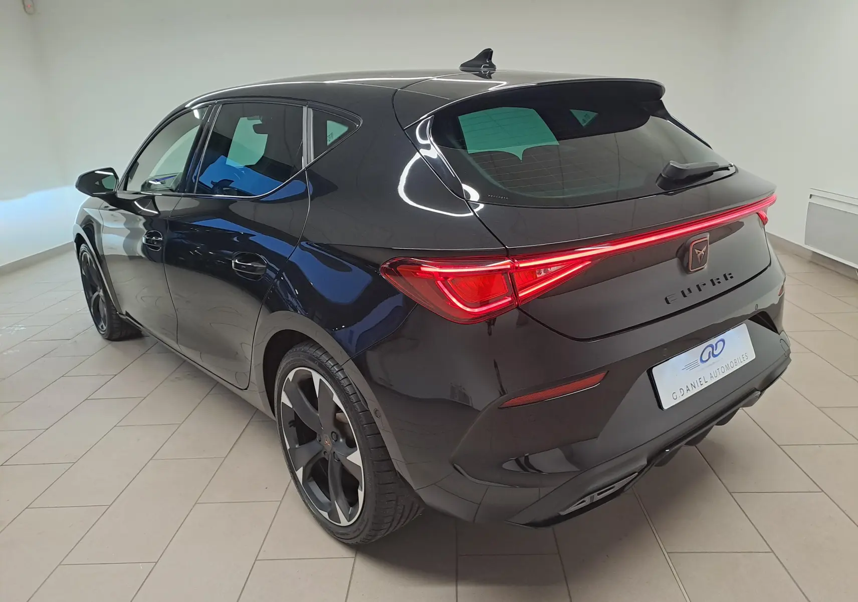 Vue 3/4 arrière droite d'une CUPRA Leon 2023 en noir minuit métallisé avec feux arrière LED et jantes noires distinctives.