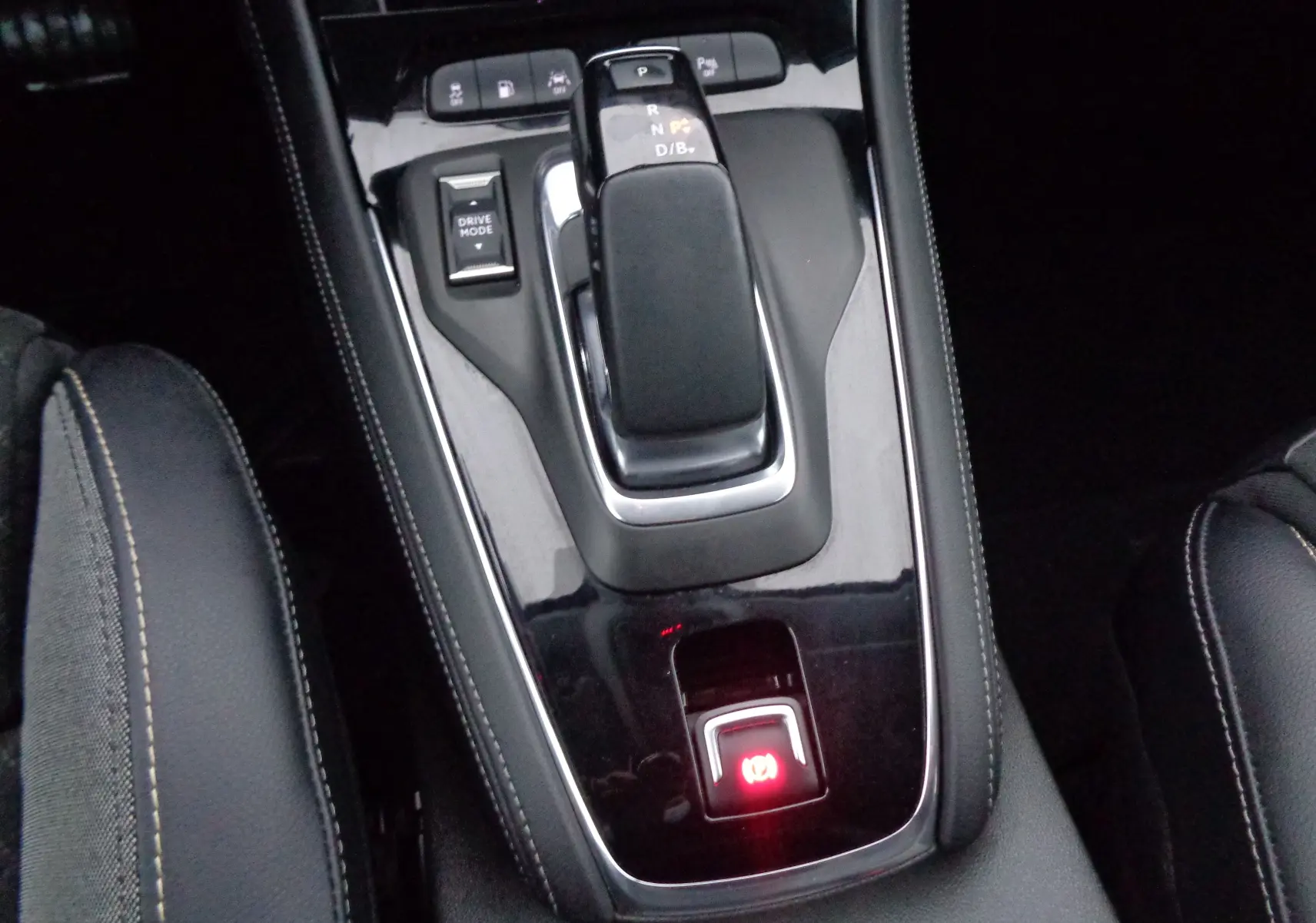 Gros plan sur la console centrale noire brillante de l'Opel Grandland X hybride, avec levier de vitesse automatique et frein à main électronique.