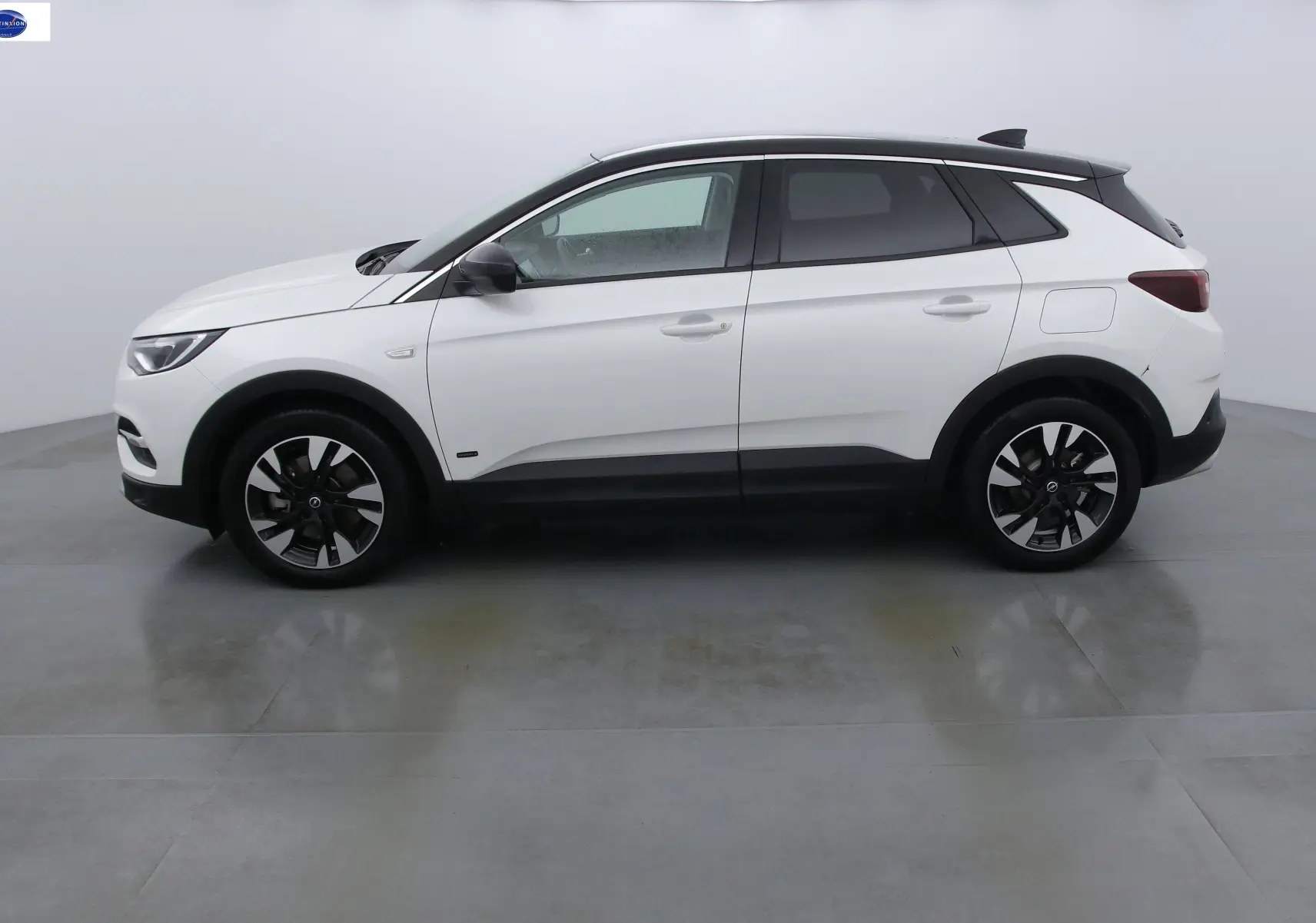 Opel Grandland X blanc métal vu de profil côté gauche, avec toit noir et jantes bicolores distinctives.