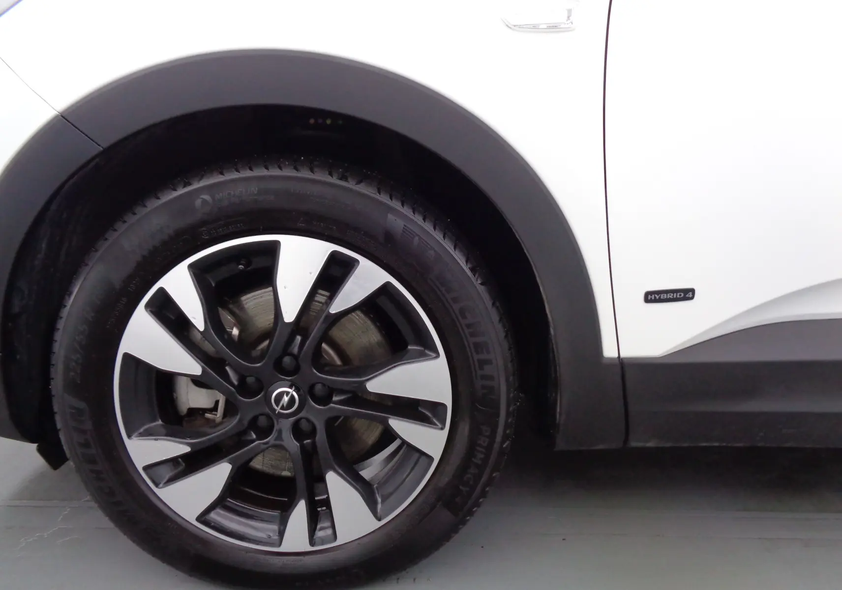 Gros plan sur la roue avant gauche et la carrosserie blanche métallisée d’un Opel Grandland X hybride rechargeable.