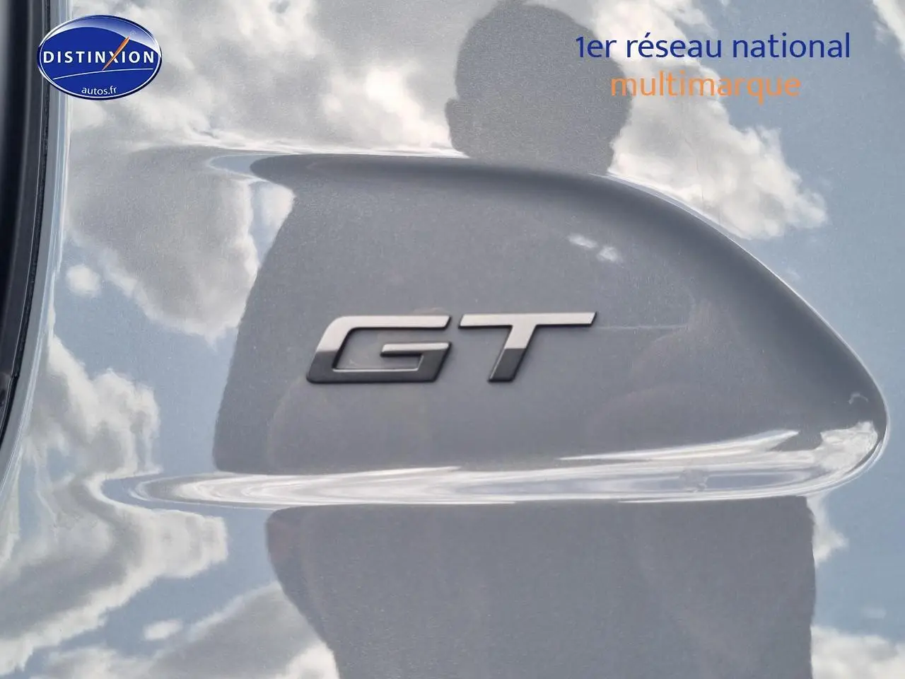 Gros plan sur l’inscription GT en relief sur la carrosserie grise métallisée d’une Peugeot 208 1.2 hybrid 136 GT.