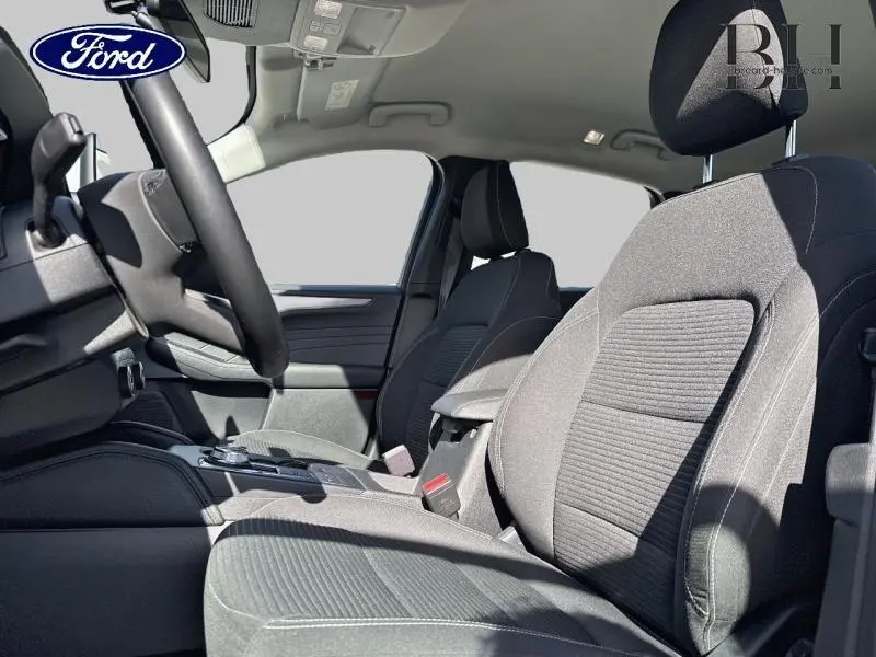 Intérieur avant du Ford Kuga 2022 gris, sièges sport en tissu noir avec volant cuir multifonction visible côté gauche