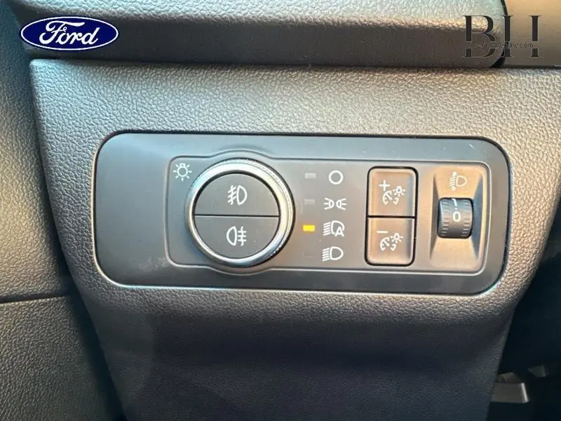 Gros plan sur les commandes d'éclairage du tableau de bord du Ford Kuga gris, avec réglage des phares et feux antibrouillard.