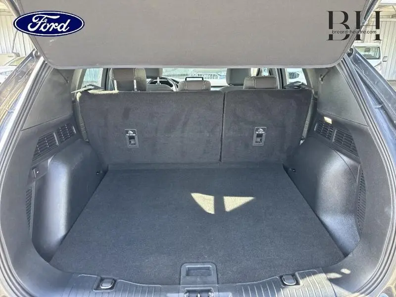 Coffre ouvert du Ford Kuga 2022 gris métallisé, montrant un espace de chargement propre et spacieux avec banquette arrière en tissu noir.