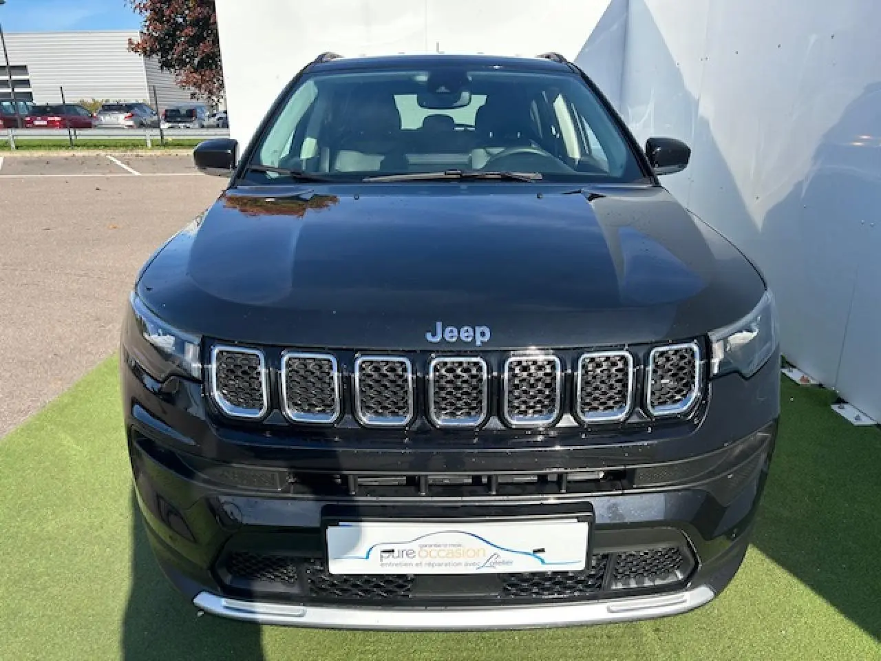 Vue avant d'un Jeep Compass noir métallisé avec calandre chromée et feux LED, stationné sur un tapis vert.