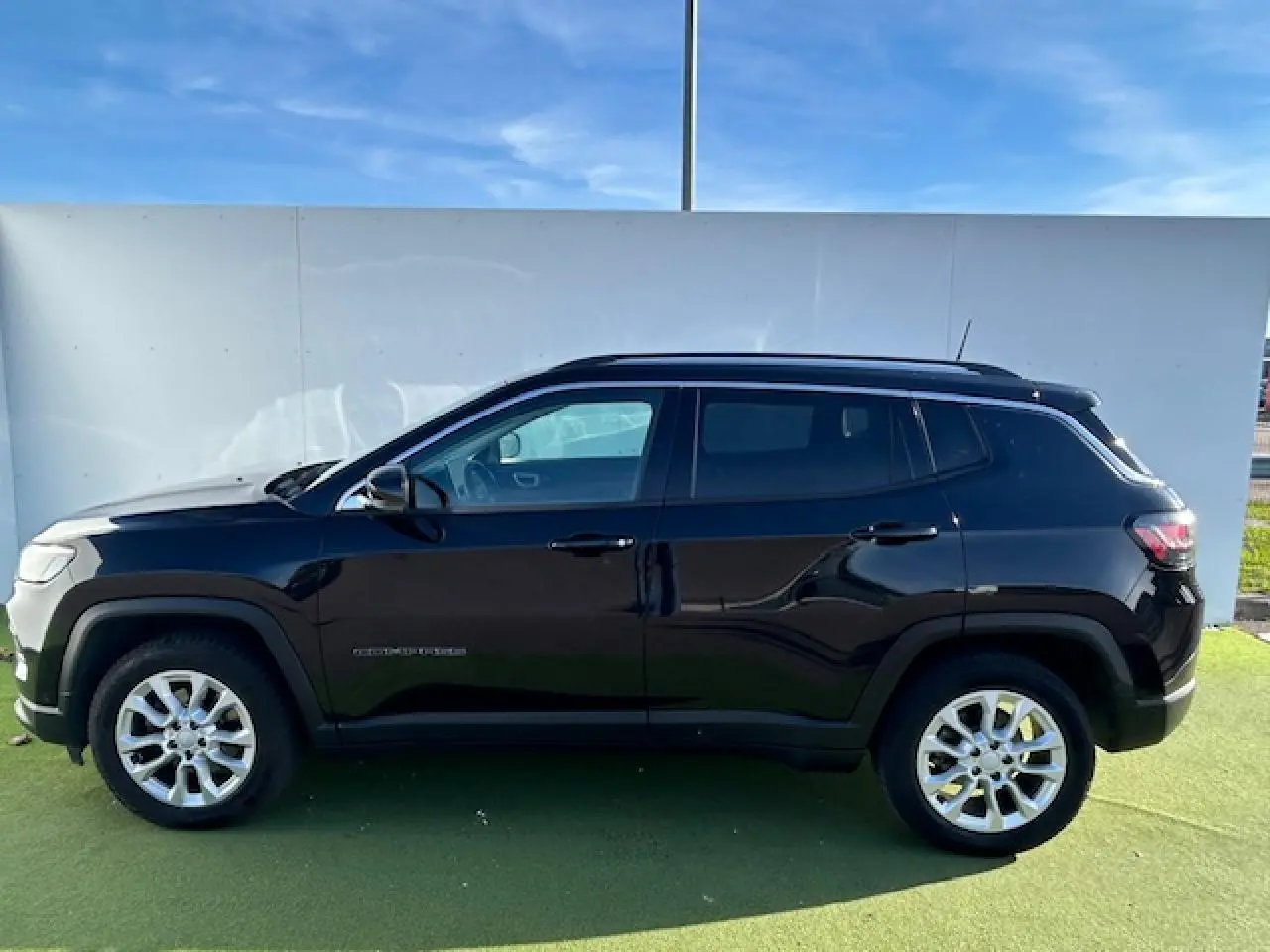 Jeep Compass noir métallisé vu de profil côté gauche, avec jantes alliage 17 pouces et barres de toit longitudinales.