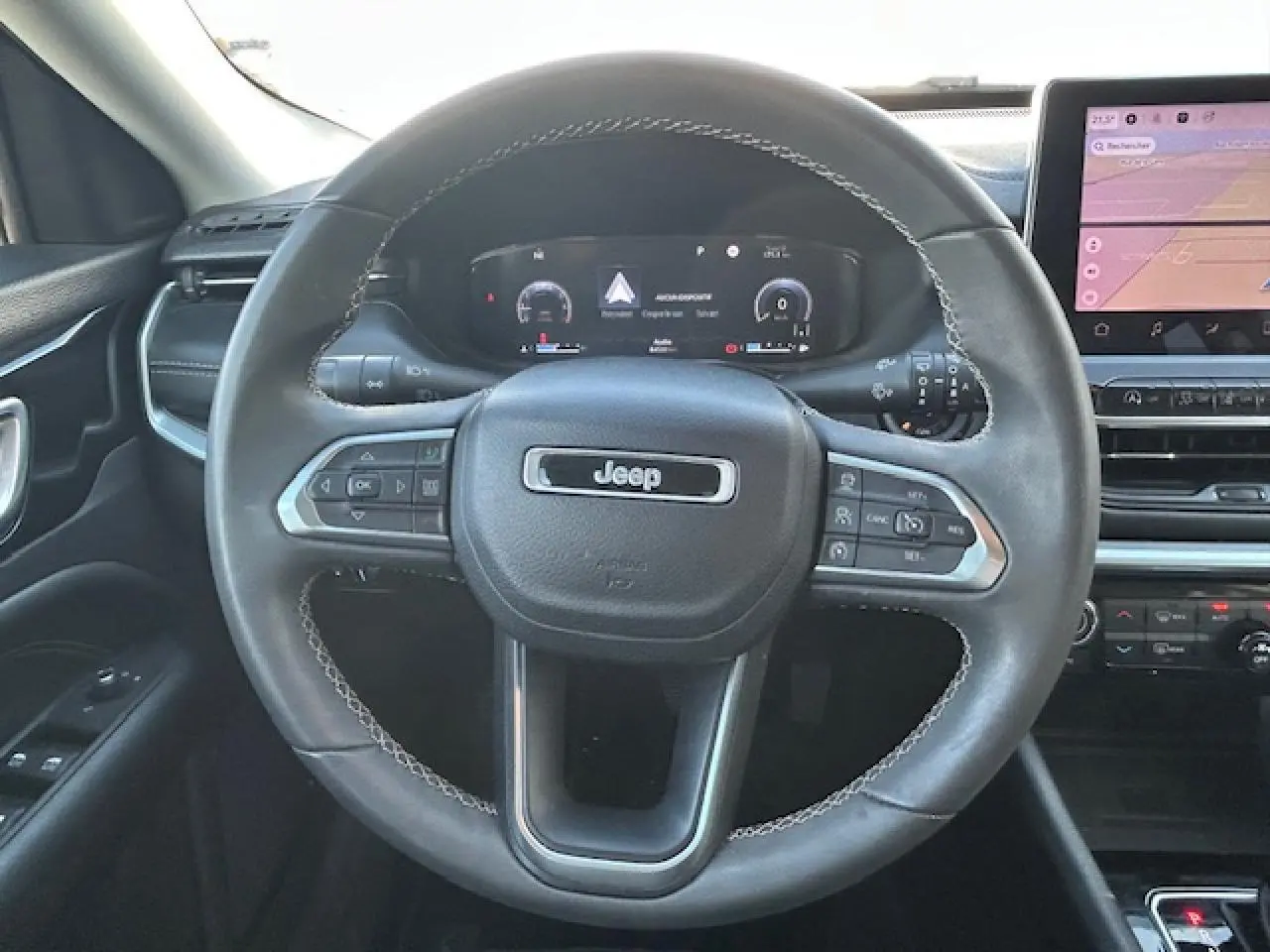 Vue intérieure centrée sur le volant cuir noir du Jeep Compass 2021 avec tableau de bord numérique et écran tactile.