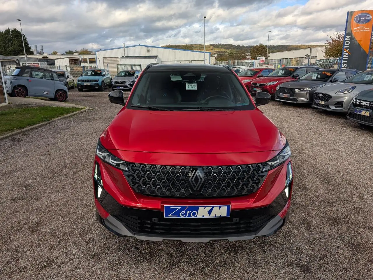 Vue avant d'un Renault Austral rouge métallisé avec calandre noire et feux LED distinctifs sur un parking.