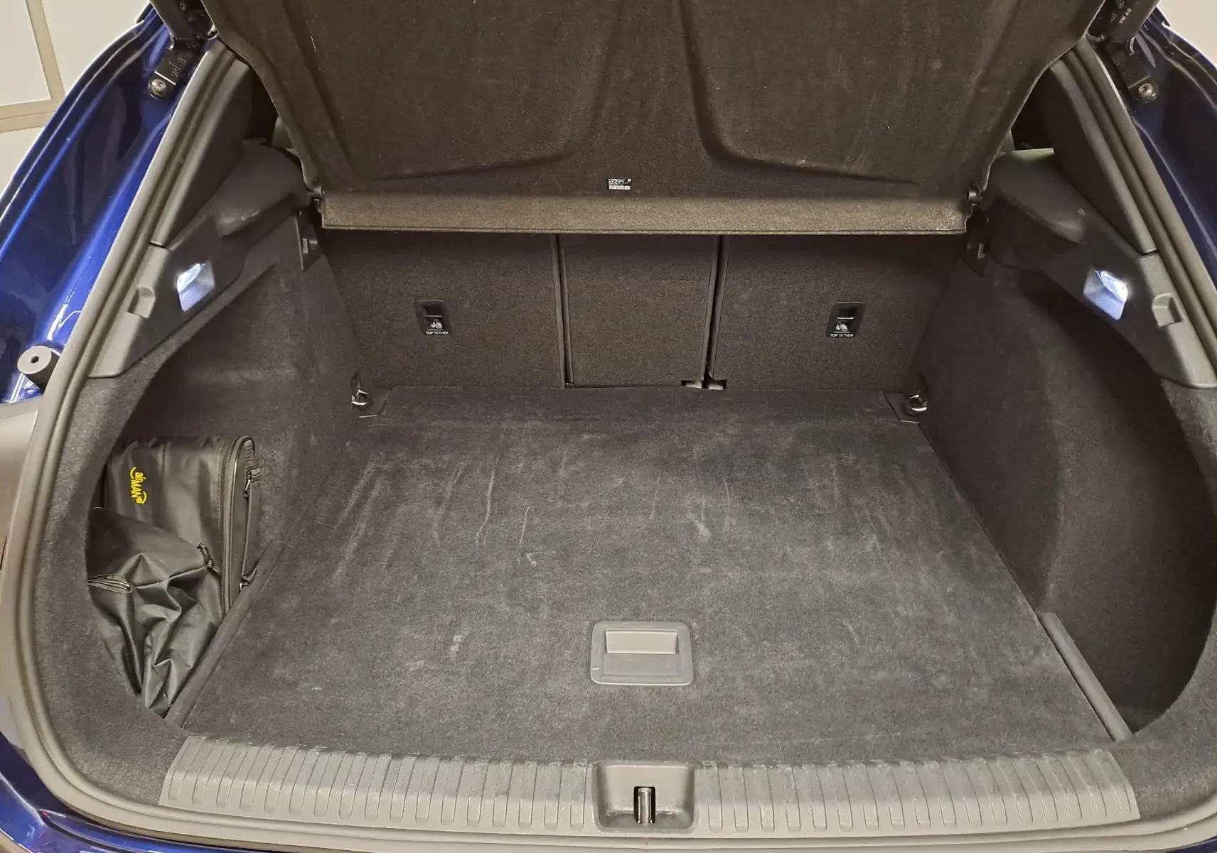 Vue du coffre ouvert du CUPRA TERRAMAR bleu Cosmos, montrant l'espace de chargement et la moquette noire intérieure.