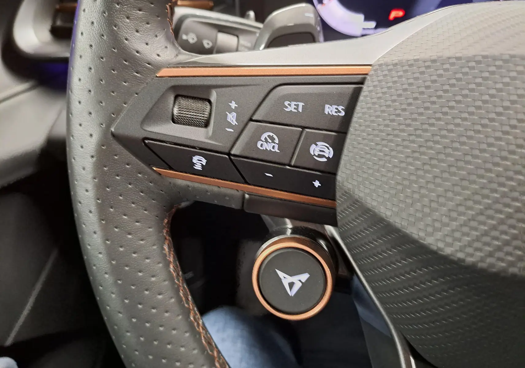 Gros plan sur la partie gauche du volant perforé de la CUPRA TERRAMAR avec commandes et logo cuivre.