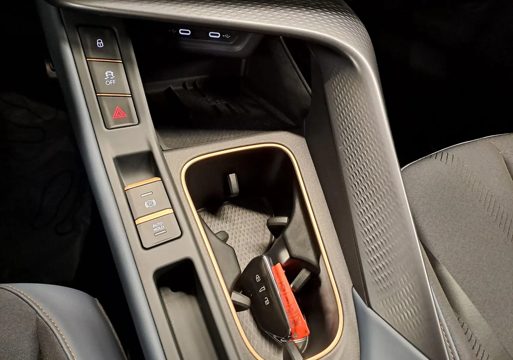 Gros plan sur la console centrale noire avec surpiqûres cuivrées et porte-clés CUPRA posé dans le porte-gobelet.