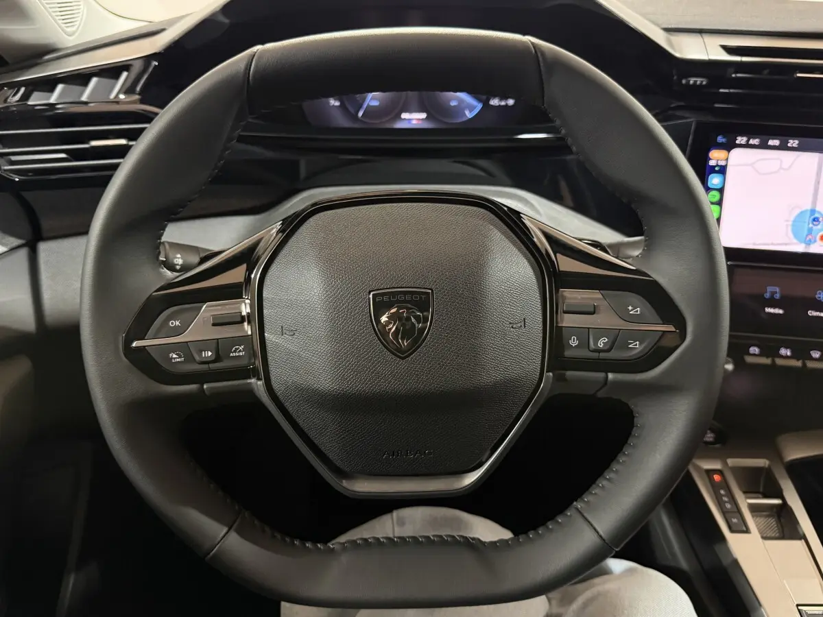 Vue centrée sur le volant cuir multifonctions de la Peugeot 308 BlueHDi 130 AUTO8 Allure, tableau de bord et écran tactile visibles.