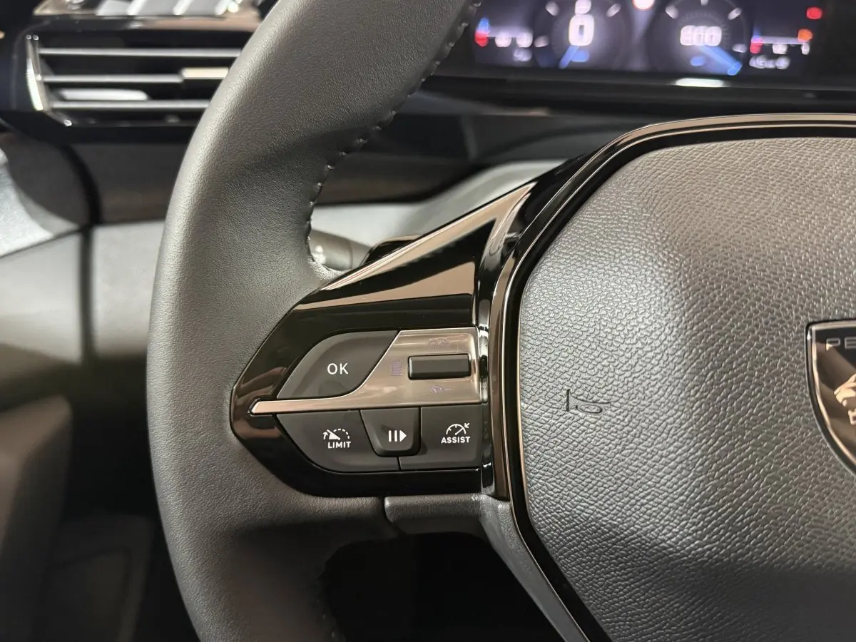 Gros plan sur le volant cuir multifonctions de la Peugeot 308 rouge, avec commandes de régulateur et assistant.