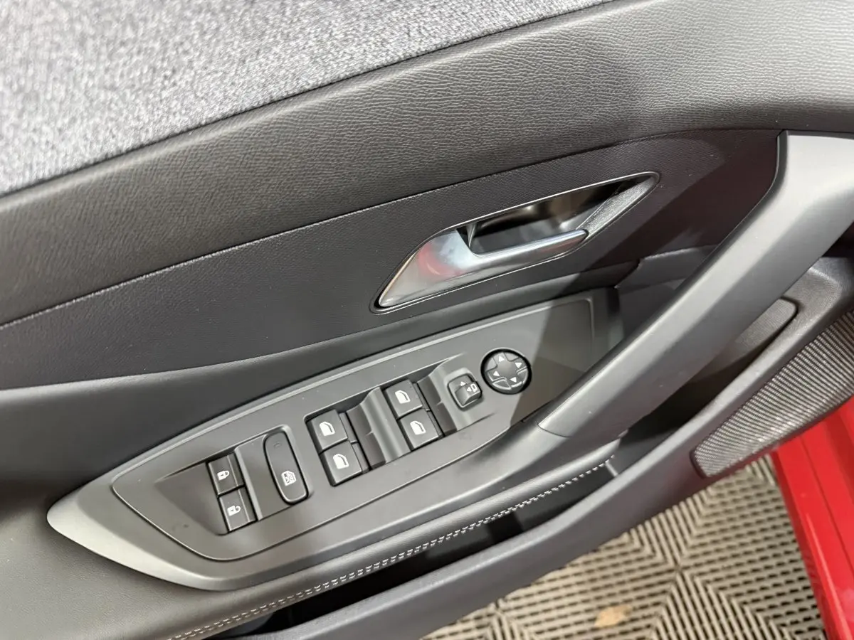 Vue rapprochée de la porte côté conducteur de la Peugeot 308 rouge, avec commandes électriques des vitres et rétroviseurs.
