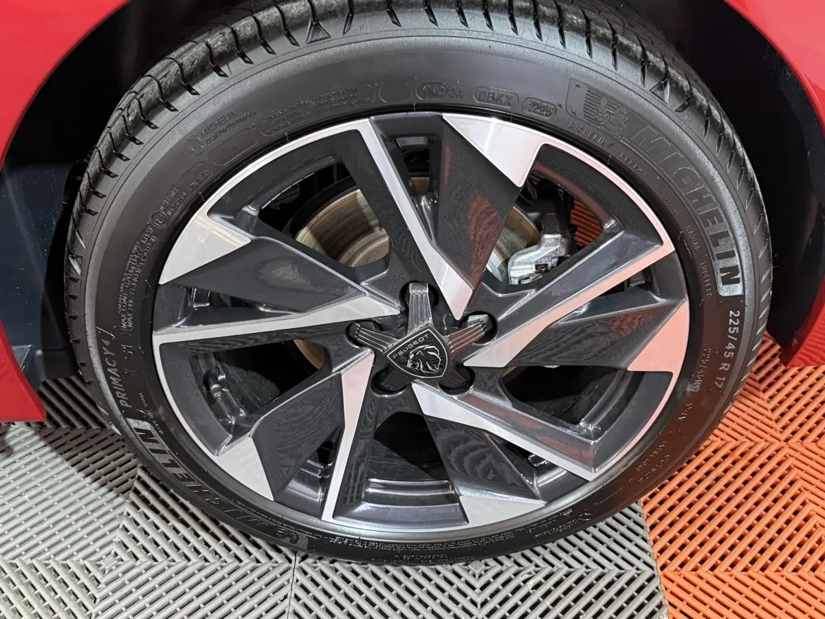 Gros plan sur la jante alliage bicolore et pneu Michelin d’une Peugeot 308 rouge, côté avant droit.