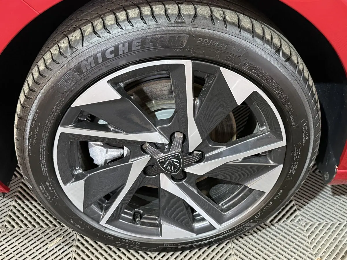 Gros plan sur la jante noire et argentée de la Peugeot 308 rouge, mettant en valeur le logo central et le pneu Michelin.