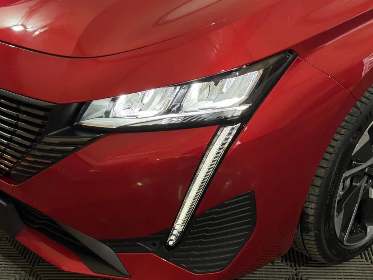 Gros plan sur l'avant droit rouge de la Peugeot 308 2025 avec phares LED et partie de la roue visible.