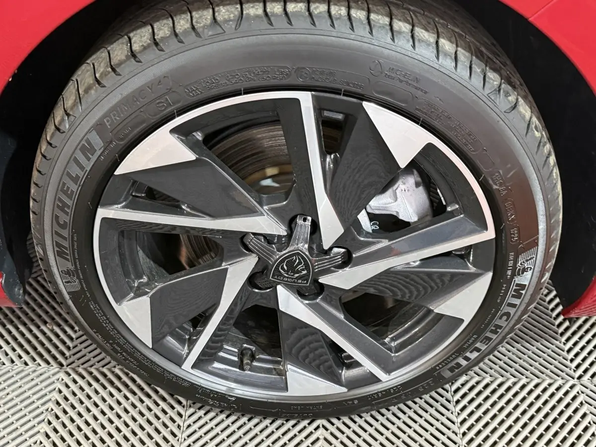 Gros plan sur la jante alliage bicolore d’une Peugeot 308 rouge, mettant en valeur le pneu Michelin et le logo central.