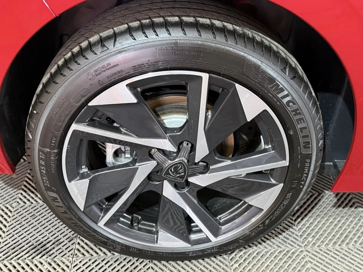 Gros plan sur la roue avant droite de la Peugeot 308 rouge, mettant en valeur la jante alliage bicolore et le pneu Michelin.