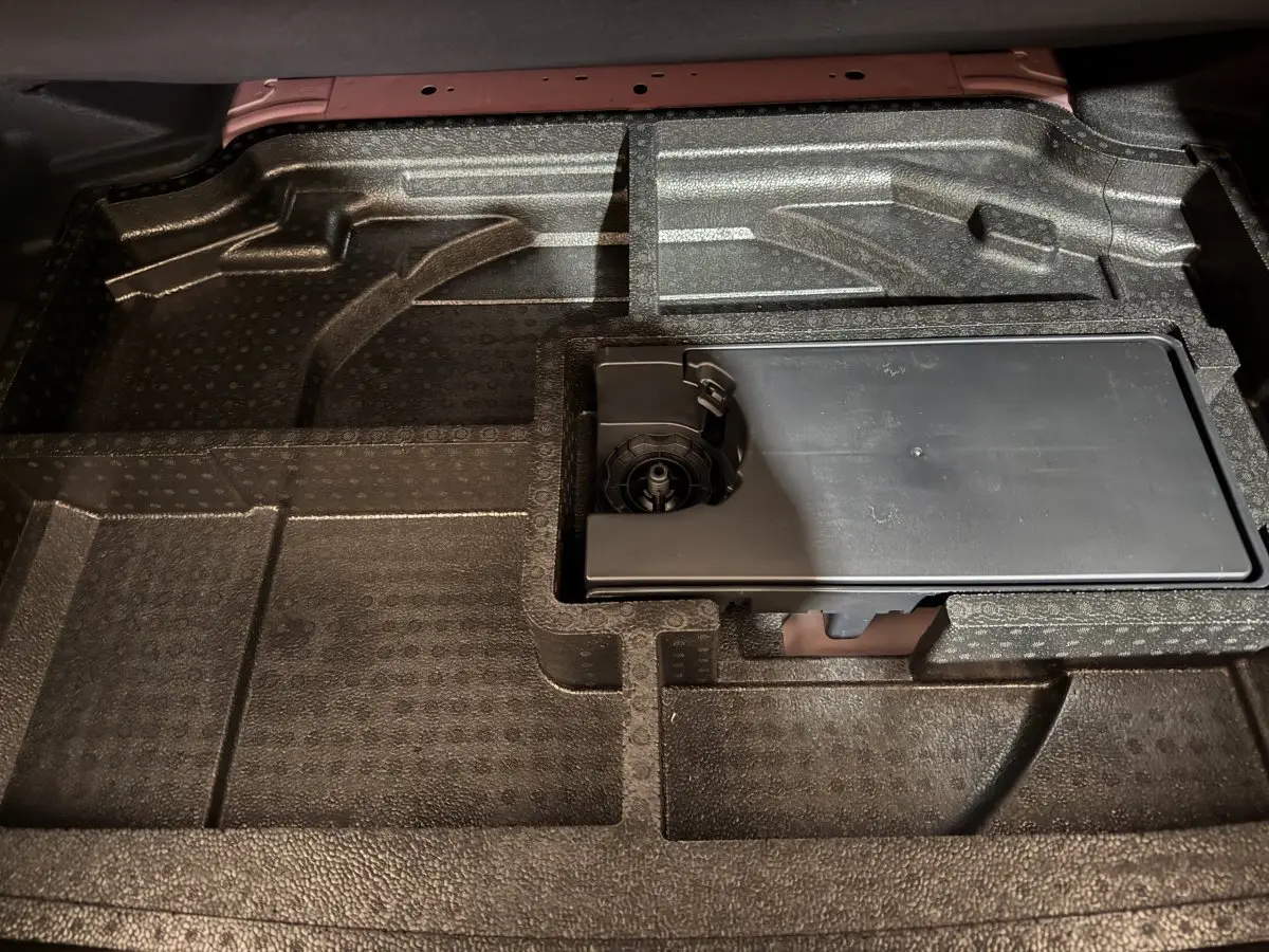 Vue rapprochée du rangement sous le plancher du coffre de la Peugeot 308 rouge, compartiments en mousse noire.