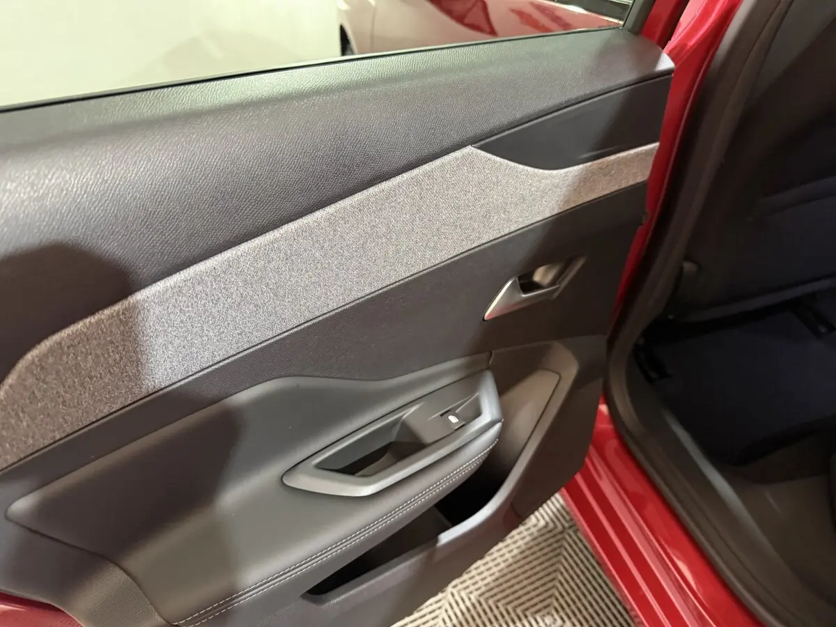 Vue intérieure côté gauche de la porte arrière rouge de la Peugeot 308 BlueHDi 130 AUTO8 ALLURE avec garniture tissu et plastique noir.