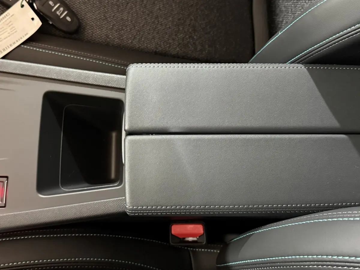 Vue rapprochée de l'accoudoir central noir avec surpiqûres bleues dans l'habitacle de la Peugeot 308 rouge 2025.