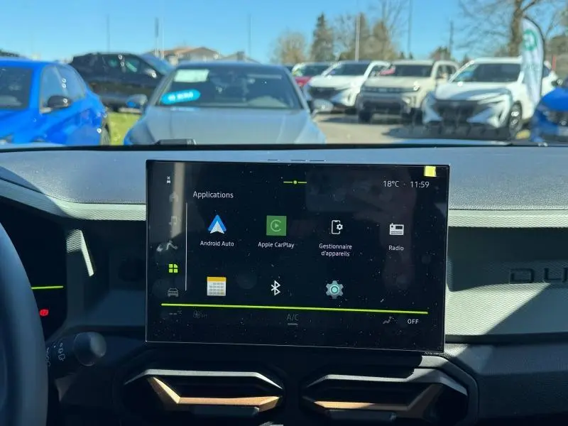 Vue intérieure centrée sur l'écran tactile multifonction du tableau de bord du Dacia Duster blanc 2025.