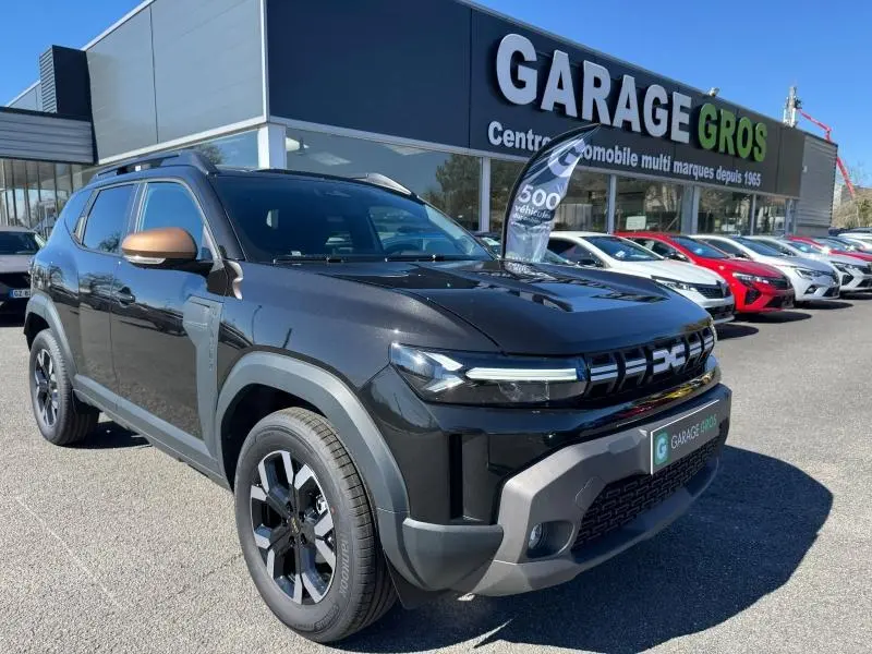 Vue 3/4 avant droite d'un Dacia Duster noir avec jantes alliage et rétroviseurs couleur bronze devant un garage.