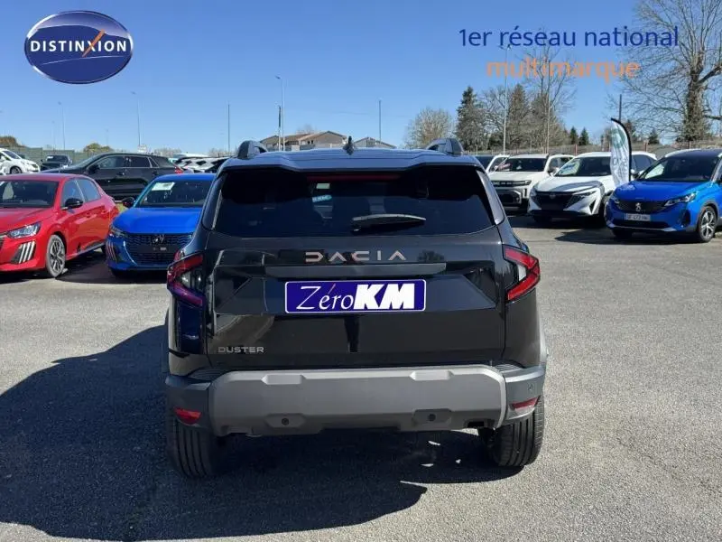 Vue arrière d'un Dacia Duster noir avec barres de toit, stationné en extérieur sur un parking.