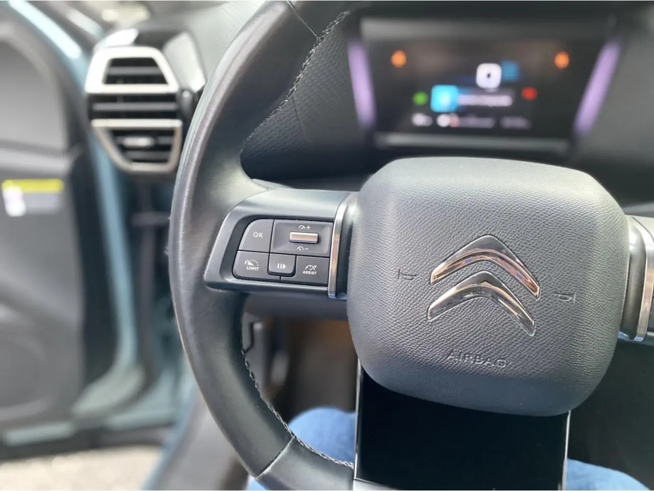 Gros plan sur le volant cuir de la Citroën C4 2021 avec commandes intégrées et tableau de bord numérique flou.