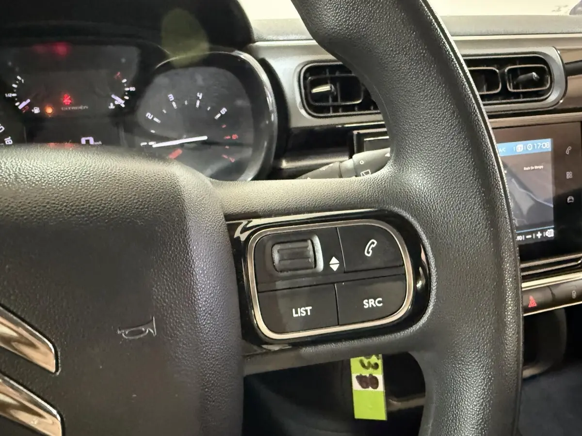 Gros plan sur le volant multifonctions noir de la Citroën C3 2021 avec commandes audio et écran tactile en arrière-plan.