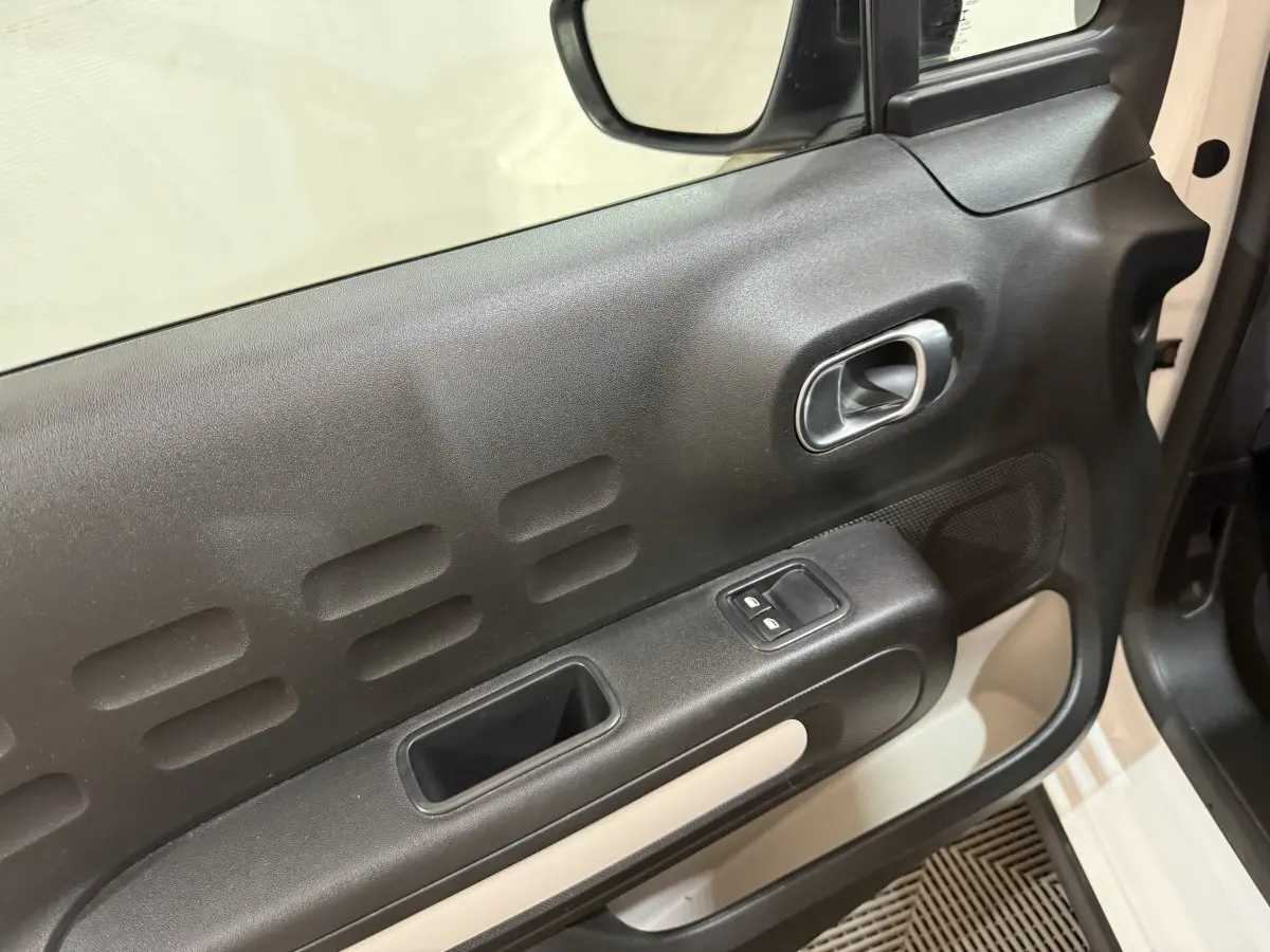 Vue rapprochée de la porte avant gauche noire et beige de la Citroën C3 blanche, avec commandes de vitres et poignée intégrée.