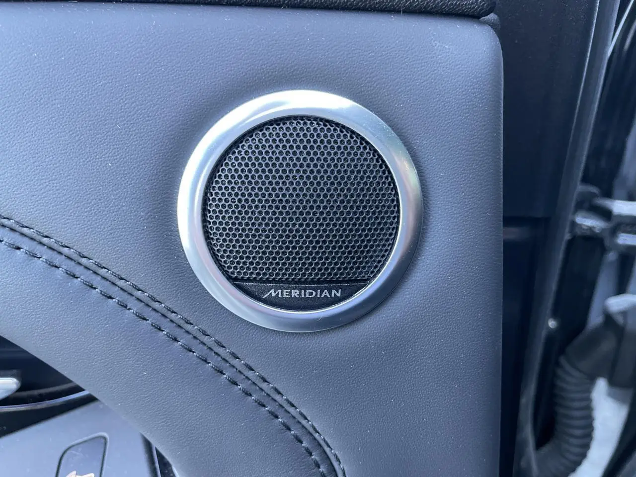 Gros plan sur l'enceinte Meridian intégrée dans la porte en cuir noir du Range Rover Evoque gris 2019.