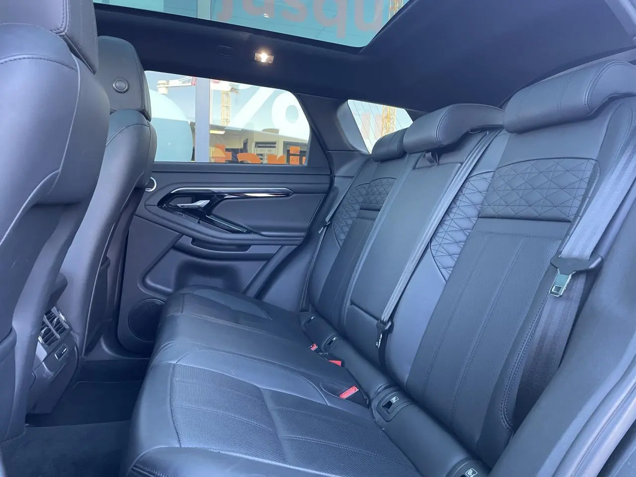 Vue latérale intérieure du Range Rover Evoque 2019 montrant les sièges arrière en cuir noir et le toit panoramique.