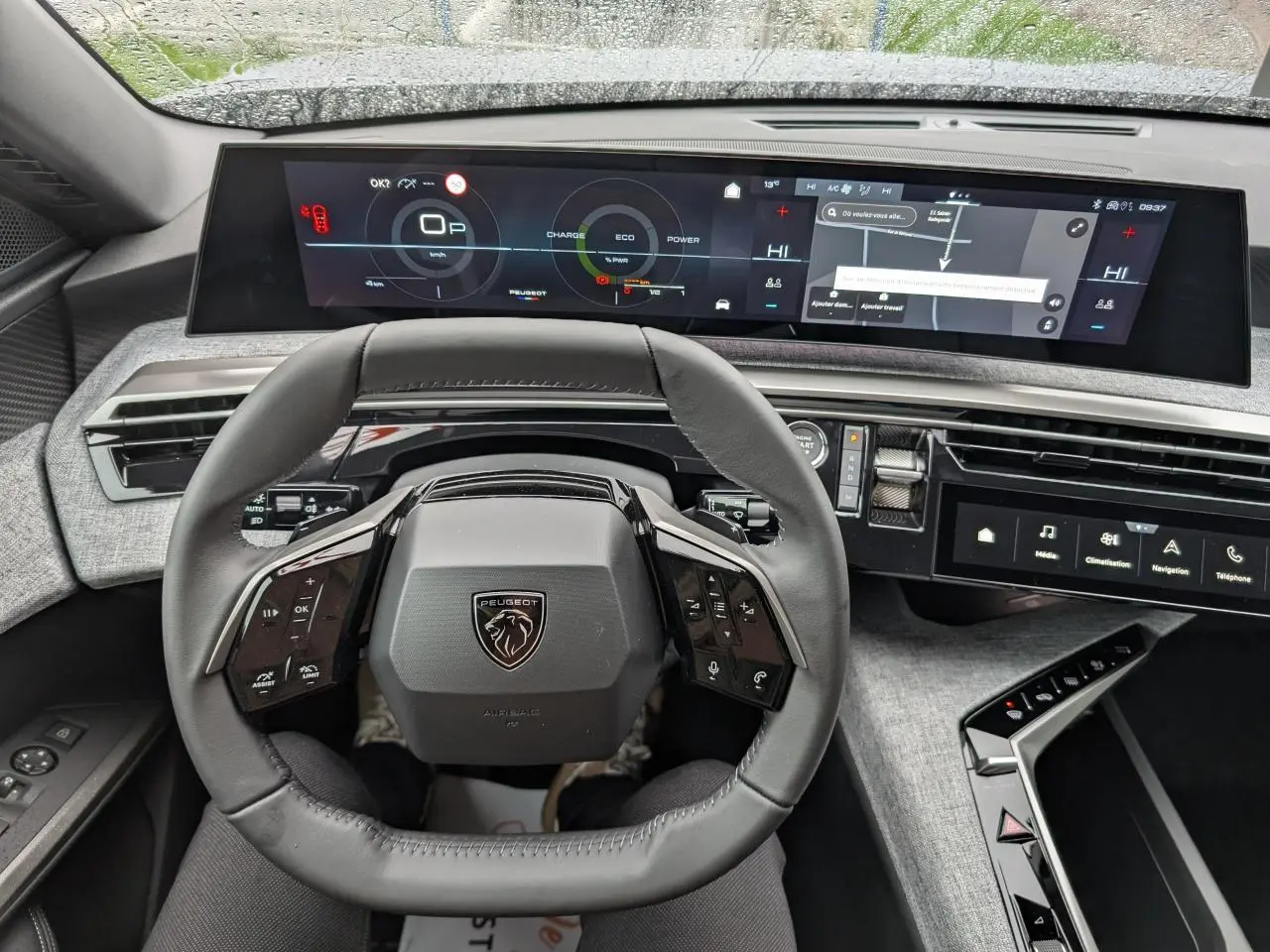 Vue intérieure du volant compact cuir et du tableau de bord numérique panoramique du Peugeot 5008 Gris Artense 2025 Allure hybride.